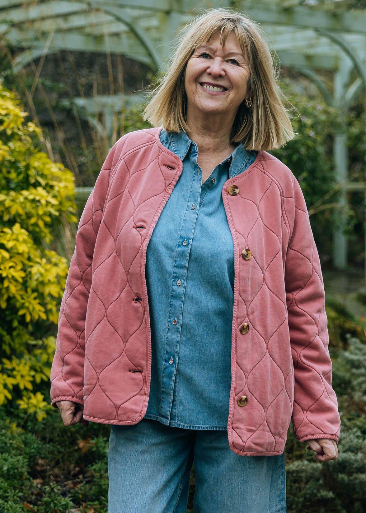 a woman in a pink jacket and jeans standing on a sidewalk